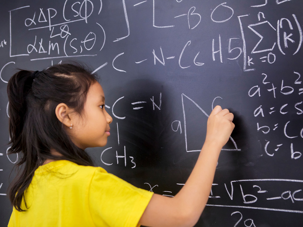 Child writing mathematical formulas on a Chameleon chalk surface
