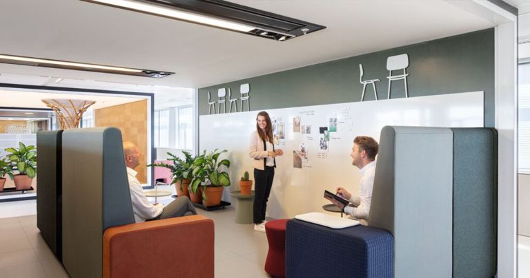 Three colleagues collaborating around a bespoke whiteboard wall in a lounge pod area