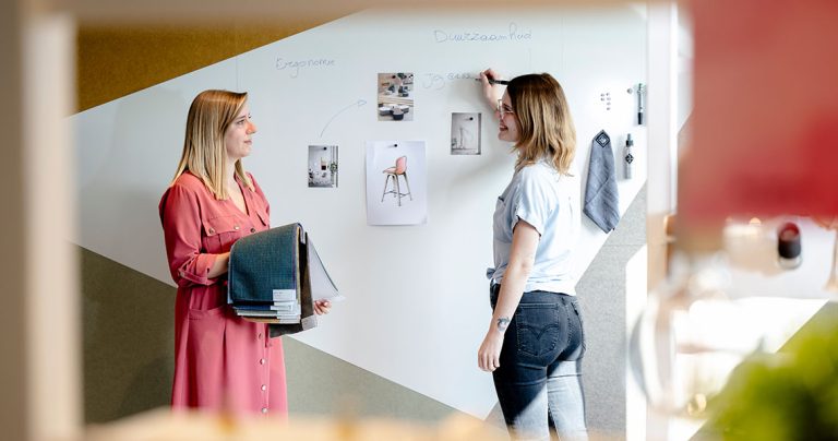 Two colleagues reviewing material swatches beside a custom-shaped whiteboard wall