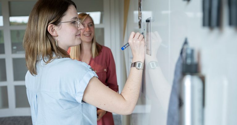 Colleague adding notes to a shared custom whiteboard wall