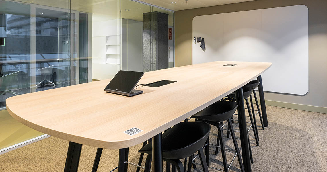 Dry erase wall panel behind a wooden meeting table with markers and eraser mounted alongside