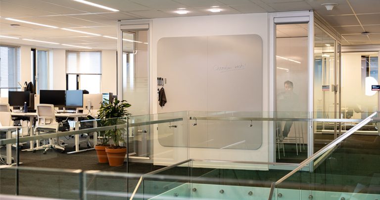 Dry erase wall panel with handwritten notes on an office mezzanine next to a glass balustrade