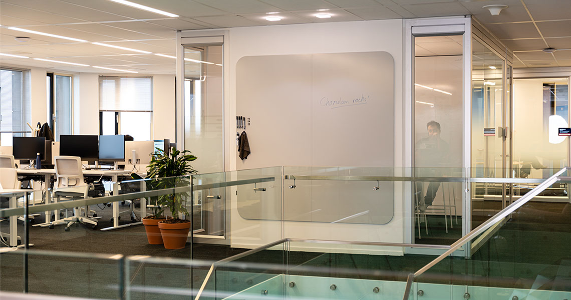Dry erase wall panel with handwritten notes on an office mezzanine next to a glass balustrade