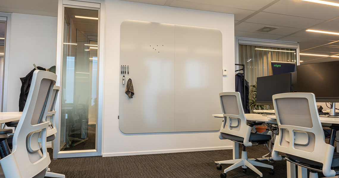 Two-panel dry erase wall with visible seam mounted on a short wall in an open-plan office