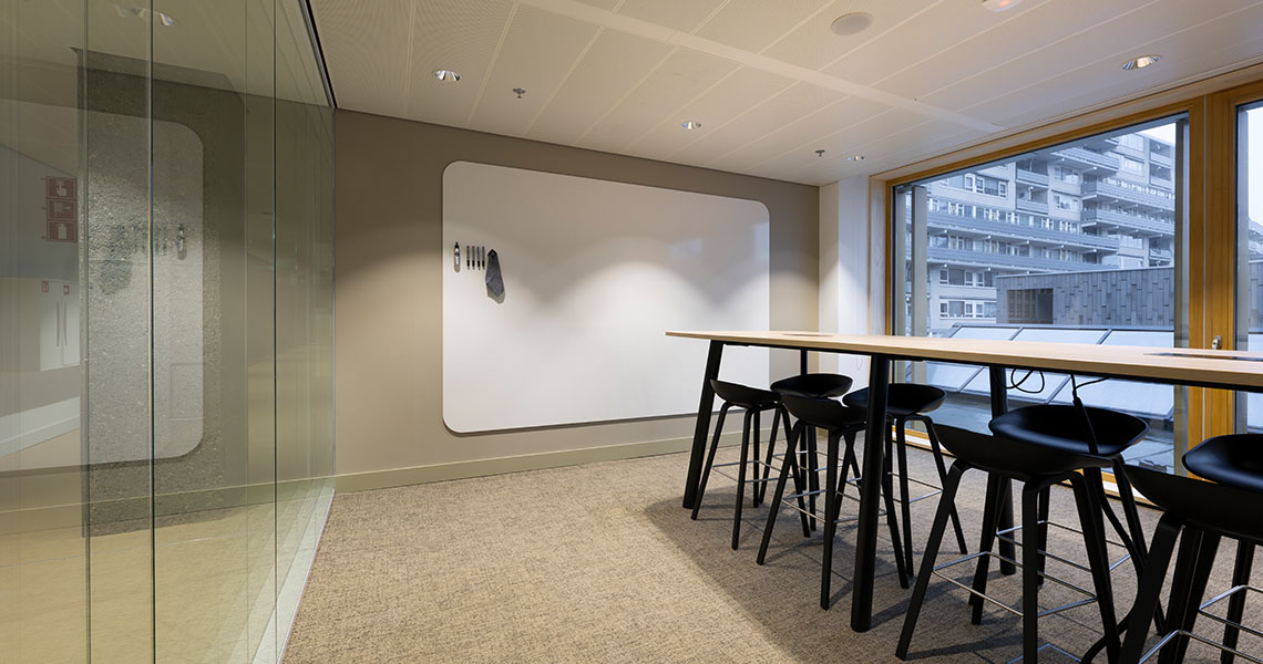 Dry erase wall panel in a glass-walled breakout room with high table and city view