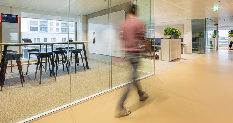 Dry erase wall panel seen through a glass-walled meeting room with high table and stools