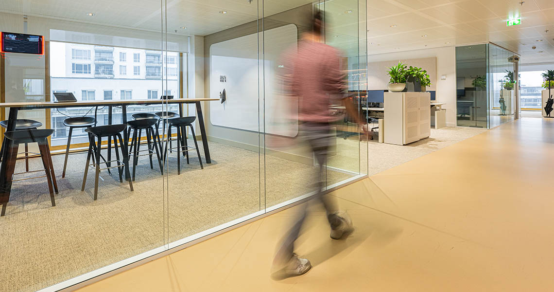 Dry erase wall panel seen through a glass-walled meeting room with high table and stools