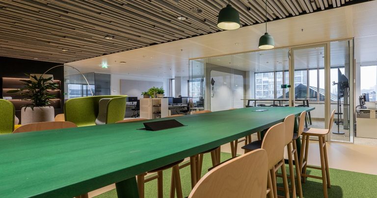 Dry erase wall panel visible through glass in a vibrant open-plan office with green high table