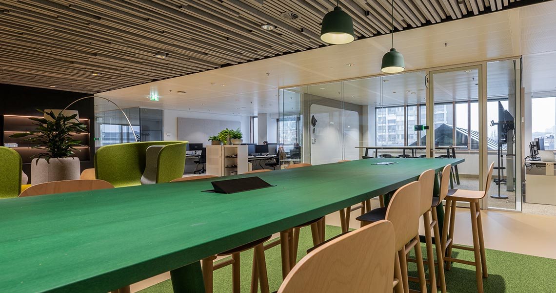 Dry erase wall panel visible through glass in a vibrant open-plan office with green high table
