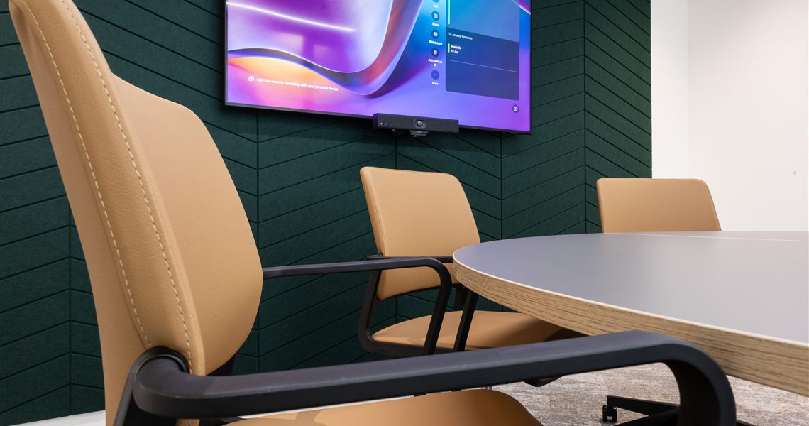 Meeting pod with a wall-mounted screen against a dark green acoustic panel wall