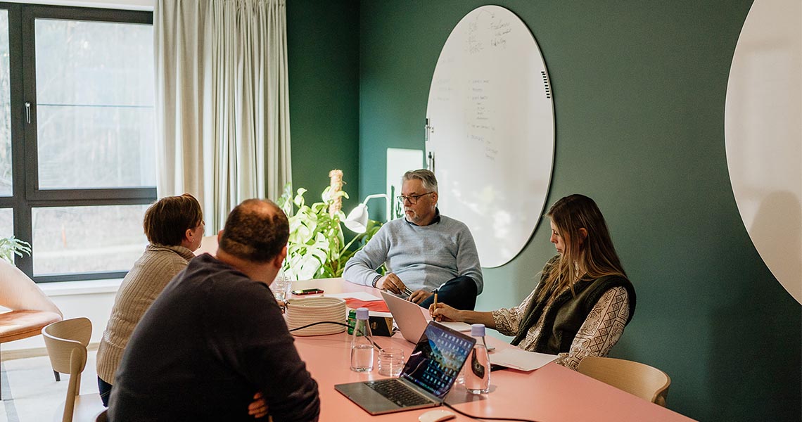 Round whiteboard on a deep green wall above a pink table in a considered, design-led meeting space