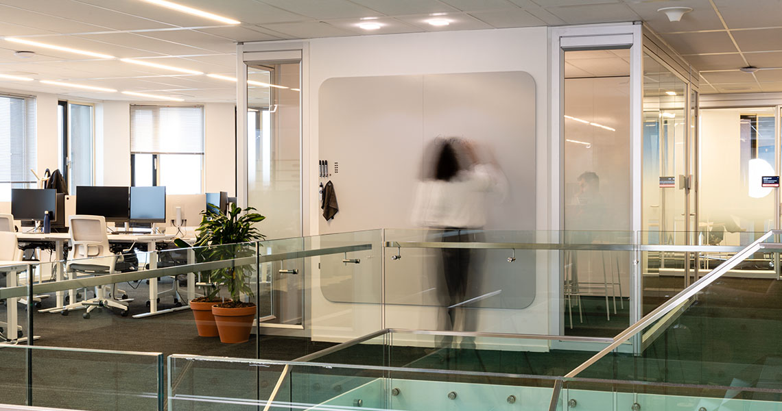 Whiteboard panel mounted between glass partitions on an open-plan office mezzanine