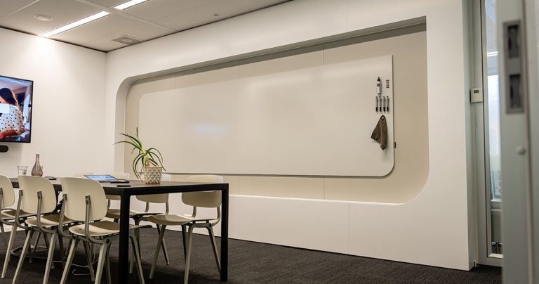 Rounded-corner whiteboard wall installed in a small meeting room with markers mounted alongside