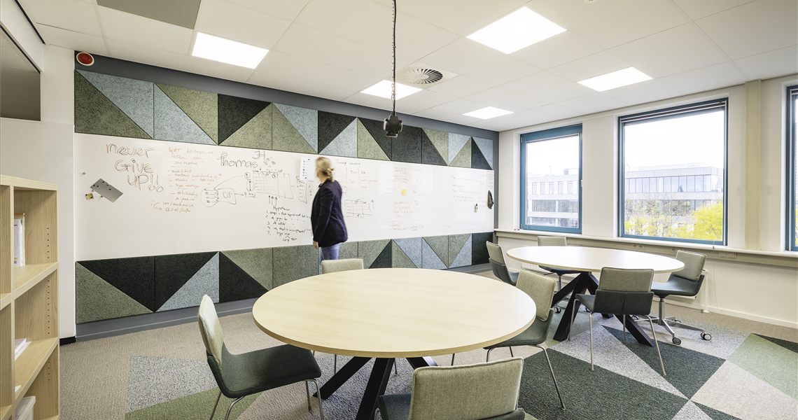 Whiteboard wall combined with a triangular acoustic panel pattern above a round table meeting area