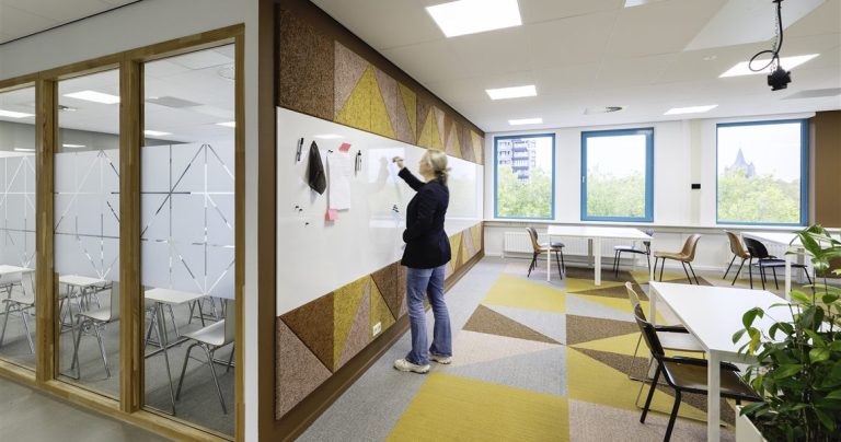 Person writing on a whiteboard wall bordered by a triangular acoustic panel pattern in a classroom