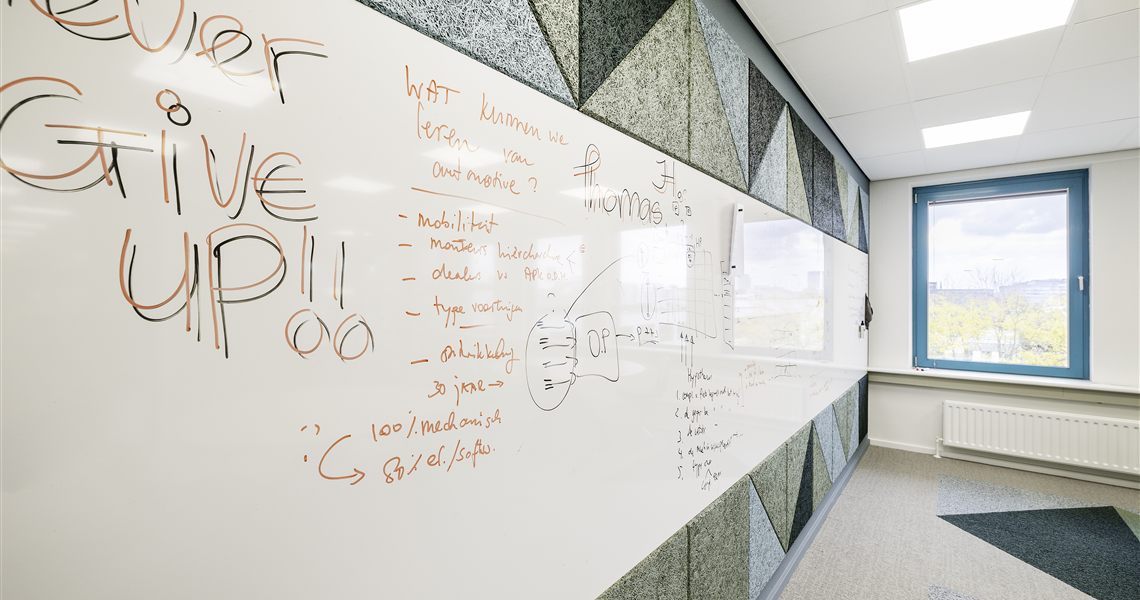 Close-up of a whiteboard wall surface meeting a triangular acoustic panel edge with handwritten notes