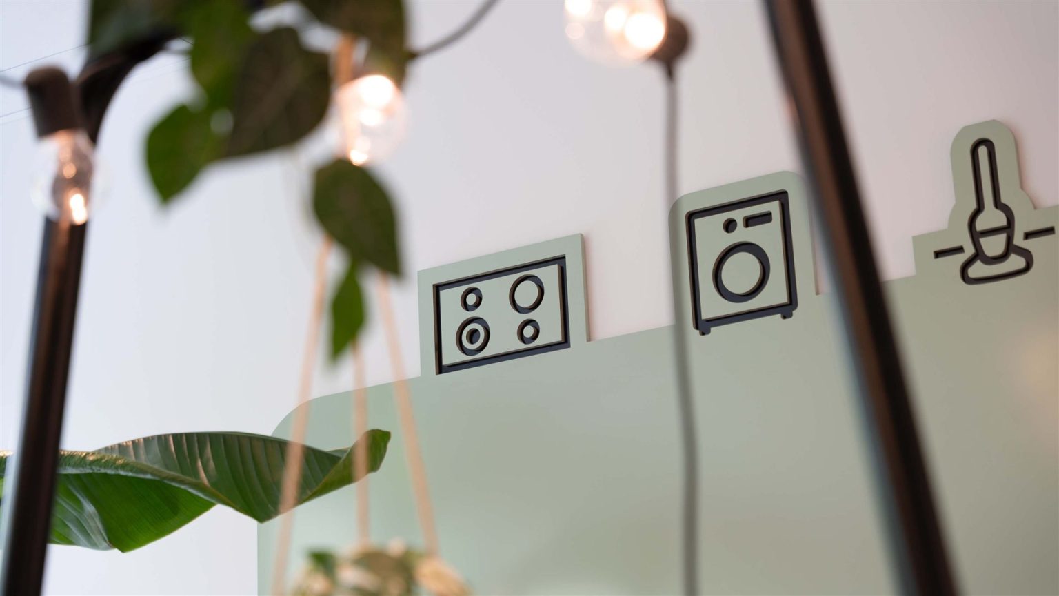 Close-up of three waterjet-cut branding icons (hob, washing machine, lamp) on sage green backing panels, an example of custom whiteboard branding.