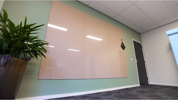 Glassboard wall panels: A blush pink Sharp Glass Wall installed across three panels in an office corridor, next to a green accent wall and a potted plant.