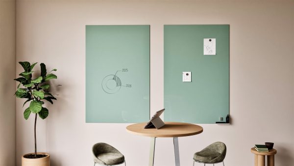 Glassboards: Two individual sage green Sharp Glassboards in an office breakout area, one with a hand-drawn chart and the other holding magnetic notes, above a round table with a tablet.