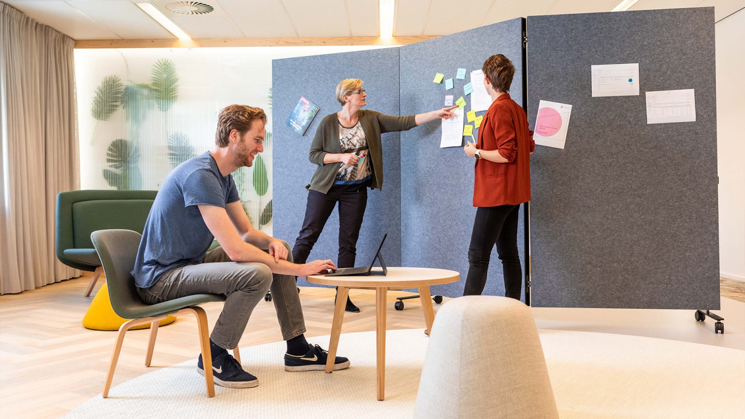 Collega's die post-its plakken op een Chameleon Harmonica Workwall met blauwgrijs akoestisch PET-vilt oppervlak