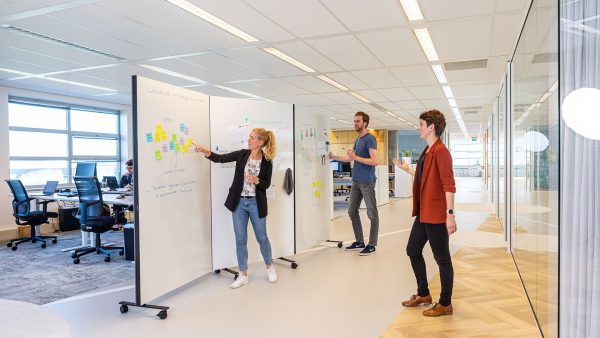 Collega's die brainstormen bij een Chameleon Harmonica Workwall met wit schrijfoppervlak in een open kantoor