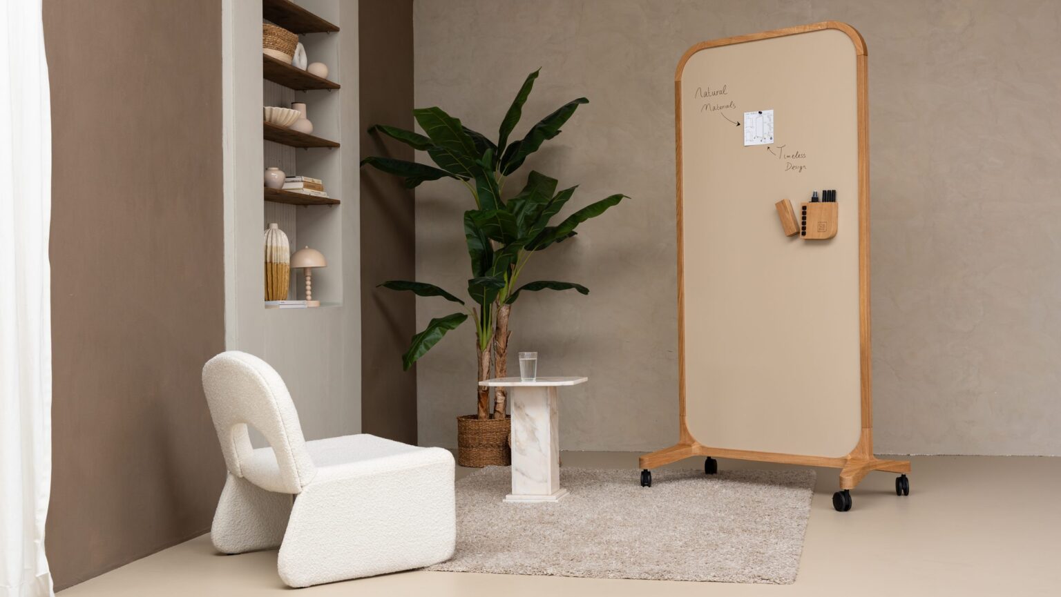 Mobiles Whiteboard auf Rollen mit weißem Sessel und Pflanze in einer Ecke